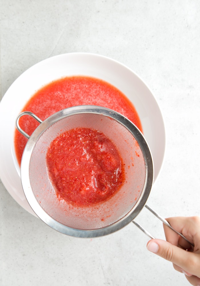 straberry coulis in strainer, with large white plate beneath