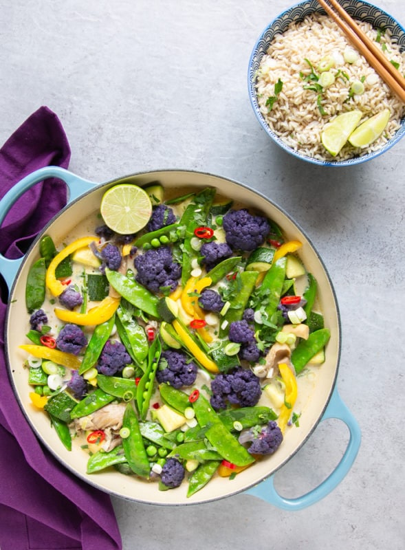 vegan thai green curry in large shallow pot with rice in a bowl and chopsticks on the side, and a purple napkin on the other side