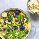 vegan thai green curry in large shallow pot with rice in a bowl and chopsticks on the side, and a purple napkin on the other side