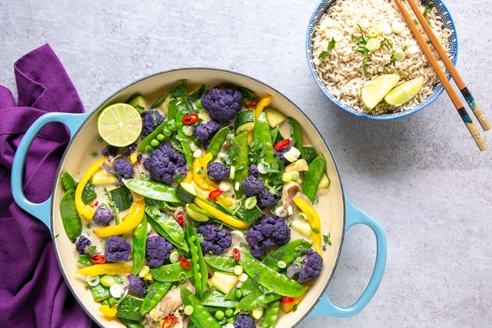 vegan thai green curry in large shallow pot with rice in a bowl and chopsticks on the side, and a purple napkin on the other side