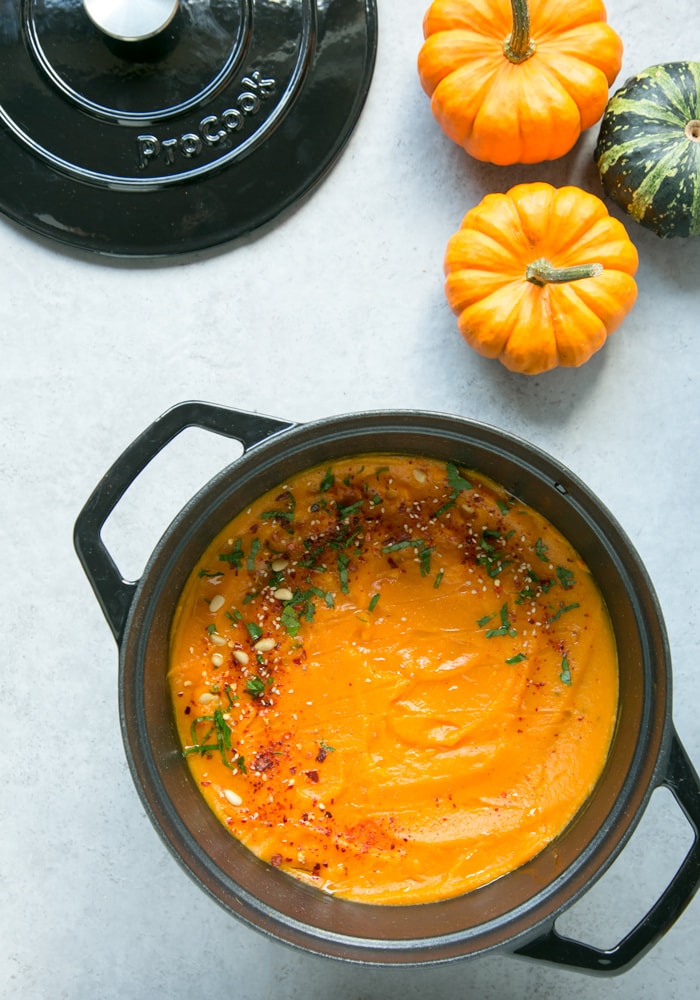pumpkin soup in casserole pot with mini pumpkins on the upper right side