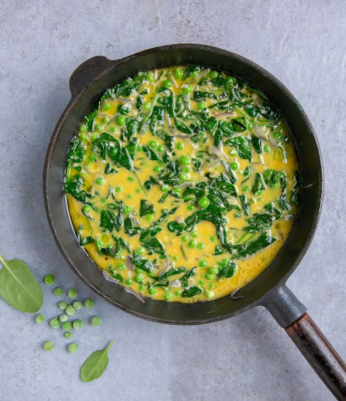 italian frittata with spinach and peas preparation step 4: frittata mixture into the cast iron skillet, spinach leaves and frozen peas next to the skillet for decoration