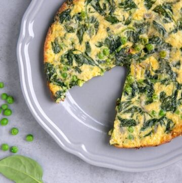 italian frittata with spinach and peas with one wedge removed on a grey plate, spinach leaves and peas on the side for decoration
