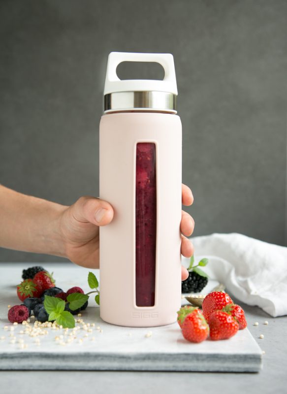mixed berry smoothie in sigg bottle in pink, grabbed by a hand , berries and a white napkin to decorate in the background