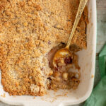 vegan apple crumble in a baking dish with golden spoon, a green napkin on the side