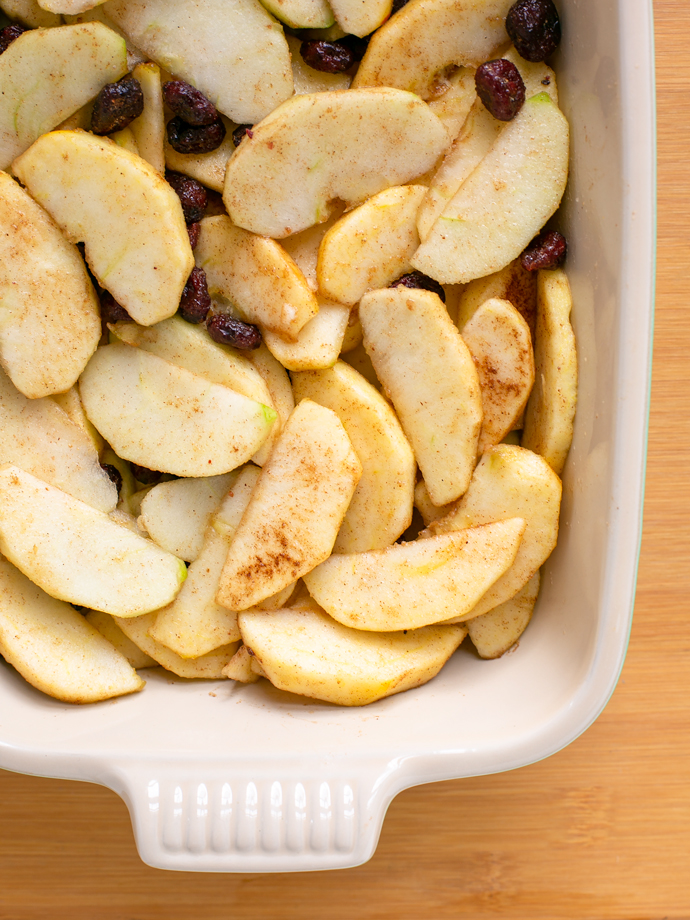 vegan apple crumble step 1: sliced apples, cranberries, spices and sugar in a baking dish