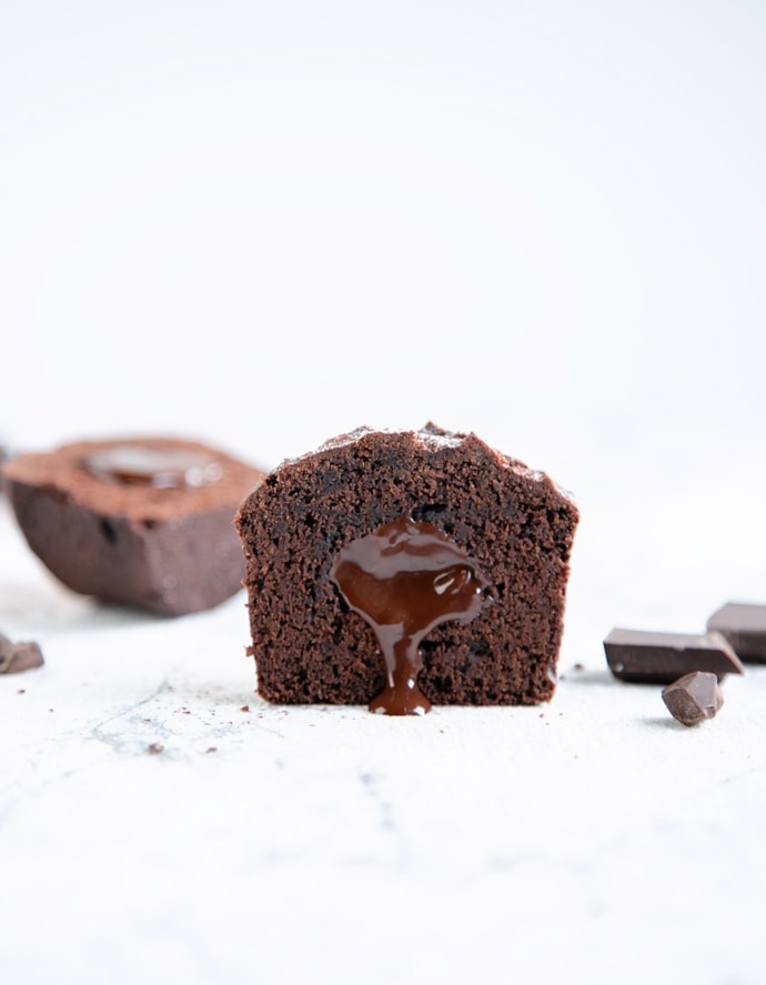 vegan chocolate muffin cut into half with chocolate pouring from the center, chocolate chunks and the remaining halved muffin in the background