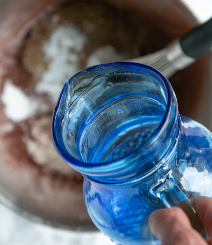 muffins recipe step 4: blue jug pouring water into the metal bowl with other ingredients