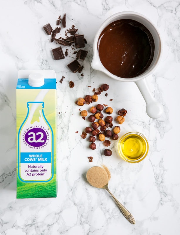 Italian chocolate hazelnut spread ingredients: a2 milk carton, hazelnuts, oil, spoon with brown sugar, chopped and melted chocolate in a white pot