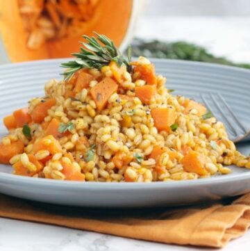 barley pumpkin risotto served on a grey plate and topped with fresh rosemary sprig.