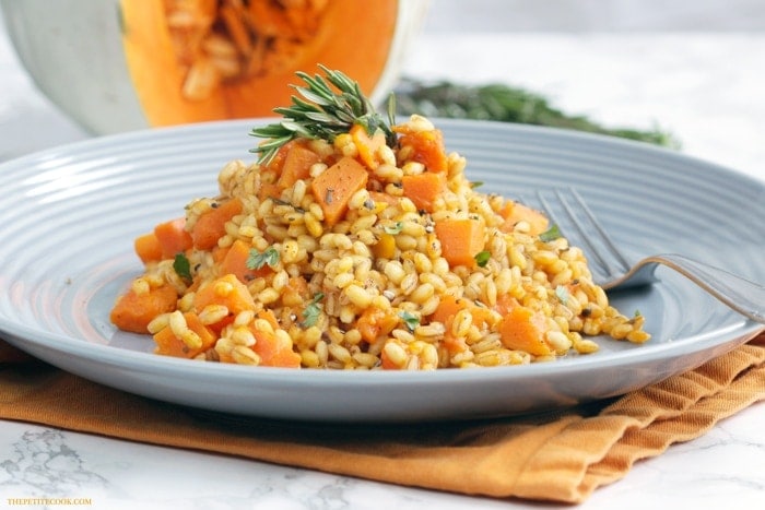barley pumpkin risotto served on a grey plate and topped with fresh rosemary sprig.