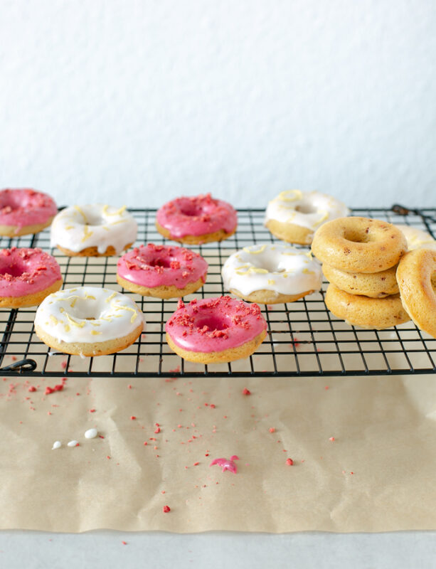 white and magenta glazed strawberry-lemon gluten-free baked doughnuts on a cooling rack, baking paper underneath