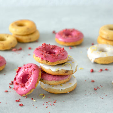 Four strawberry-Lemon gluten-free baked donuts on top of each other, one doughnut on the left side, and more doughnuts in the background