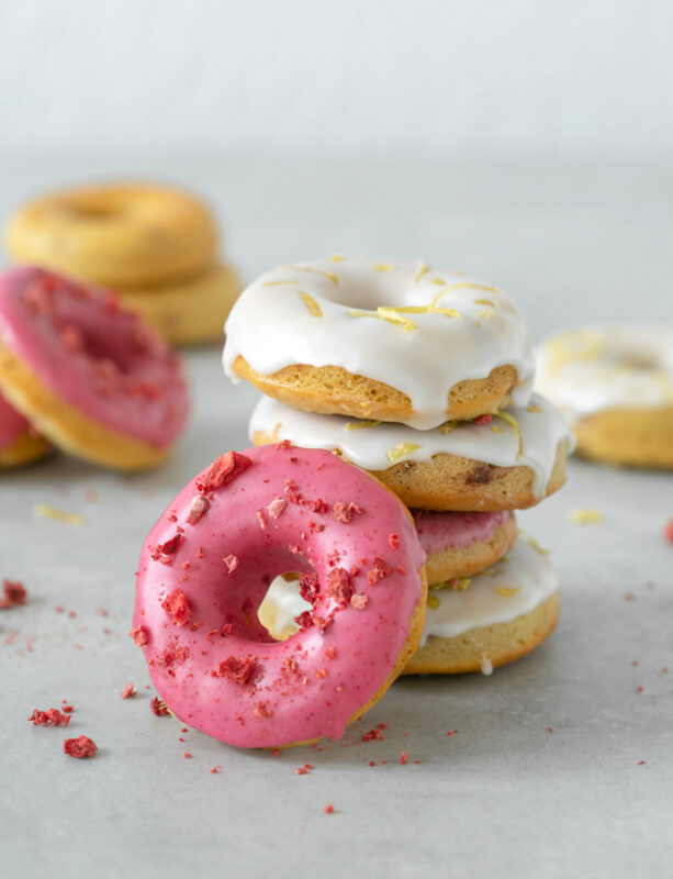 Four strawberry-Lemon gluten-free baked donuts on top of each other, one doughnut on the left side, and more doughnuts in the background
