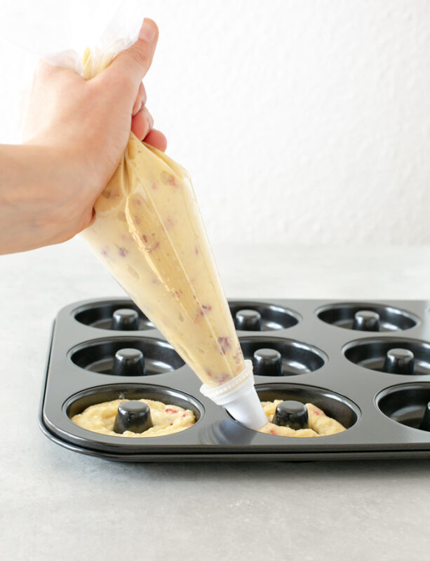 Hand holding a piping bag filled with doughnut batter, filling a doughnut pan