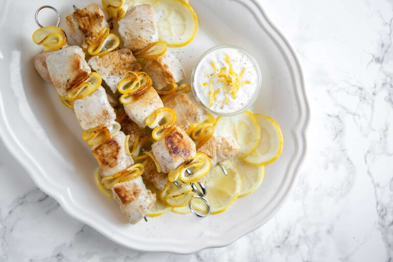 lemon chicken skewers and small pot with yogurt dip and lemon slices onto white serving plate