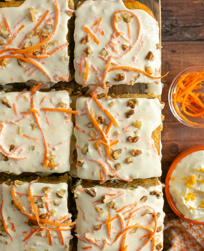 squares of carrot cake topped with mascarpone cream, sliced carrots and chopped nuts.