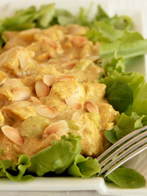 coronation chicken topped with toasted almond flakes on a bed of salad leaves