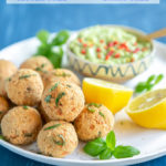 baked salmon meatballs on white plate served with halved lemon, basil leaves and avocado cream in a small pot - image optimized for pinterest