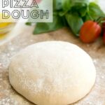 Homemade pizza dough on a wood board, tomatoes and basil in the background. Image for Pinterest.