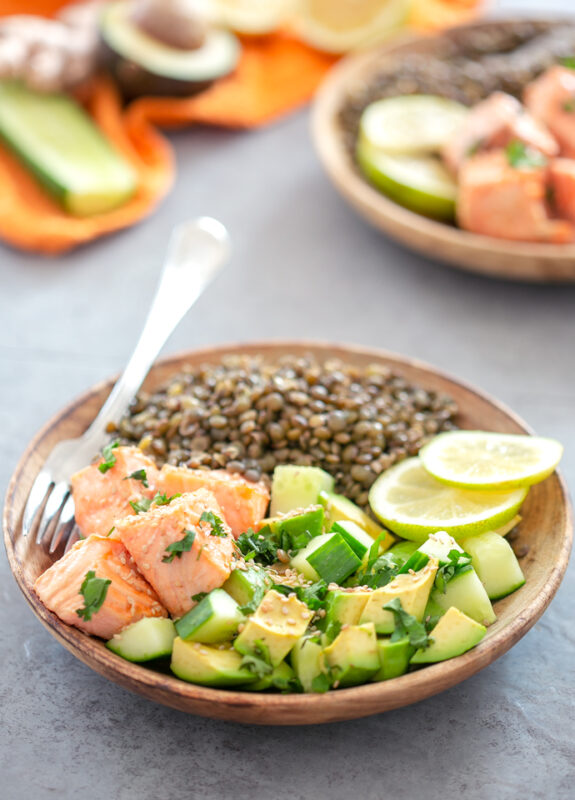Air Fryer Salmon in Coconut Milk with Lentils, avocado, cucumber and 2 slices of lemon o a wood plate with a fork. Another plate of the same recipe in the background
