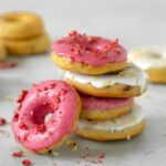 Four strawberry-Lemon gluten-free baked donuts on top of each other, one doughnut on the left side, and more doughnuts in the background