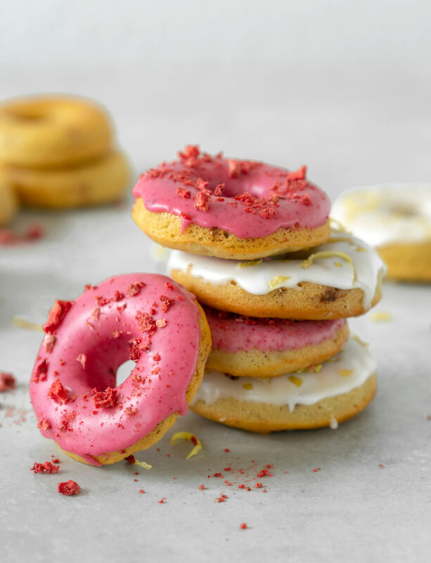 Four strawberry-Lemon gluten-free baked donuts on top of each other, one doughnut on the left side, and more doughnuts in the background