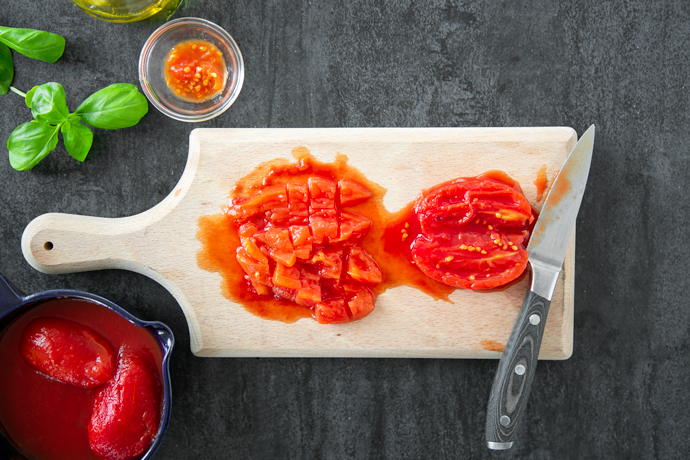 recipe step 1: chopped tomato and halved tomato with a knife on a wood chopping board, and a small bowl with the seeds removed from the tomatoes.