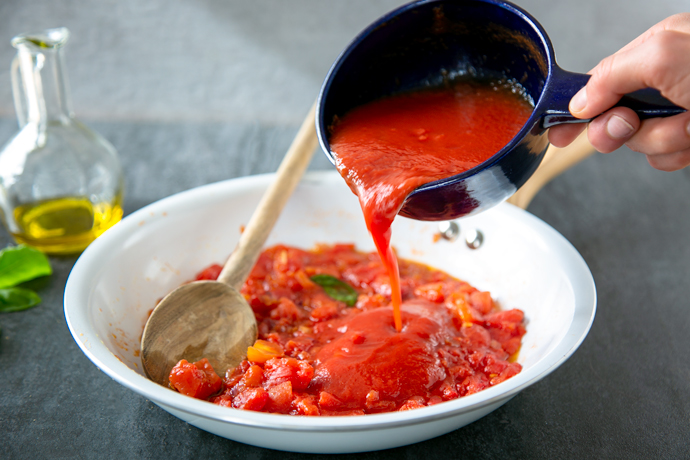 tomato sauce recipe step 3: hand pouring reserved canned tomato juice in the pan together with the other ingredients.