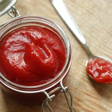 homemade ketchup in a jar, with teaspoon filled with ketchup next to it, over wood board