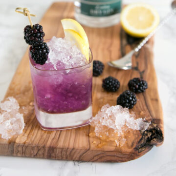 bramble cocktail topped with a slice of lemon and two blackberries secured in a skewer.