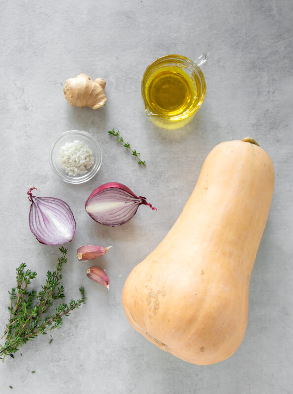 fresh thyme sprigs, 2 garlic cloves, red onion halved, sea salt in a small bowl, piece of fresh ginger, small jug with olive oil and a large butternut squash