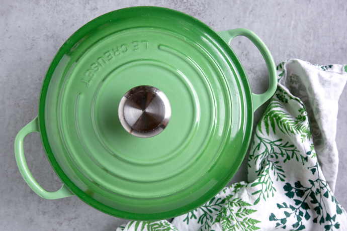 green cast iron pot with lid on top of it, next to a white and green kitchen cloth