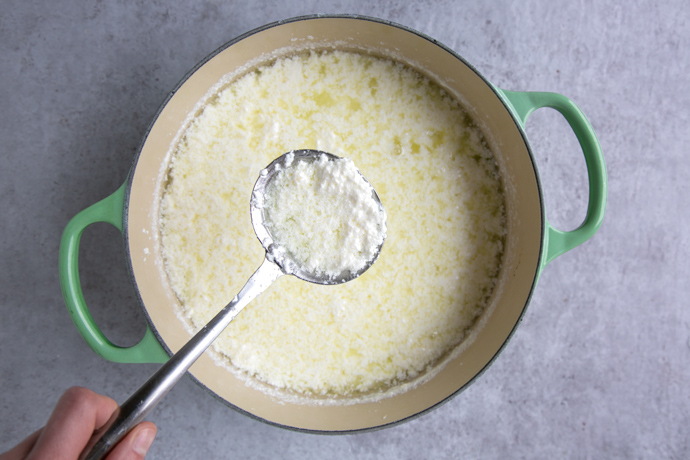 slotted spoon removing curd needed for homemade ricotta from a large cast iron pot with green handles