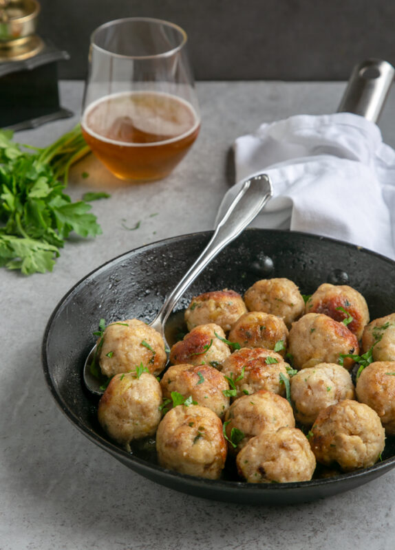 turkey meatballs in pan with spoon, white napkin that cover the pan handle, glass of beer next to the pan and bunch of fresh parsley.