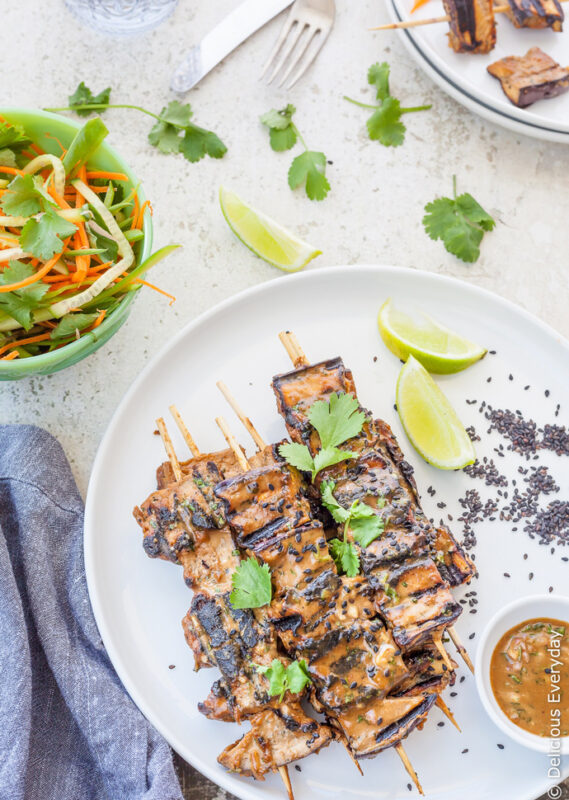 grilled eggplant kebabs served on a dish with lime wedges and tahini marinade.