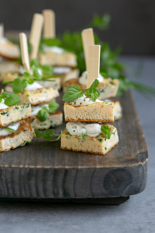 individual frittata sandwhich bites topped with fresh herbs on a wood board