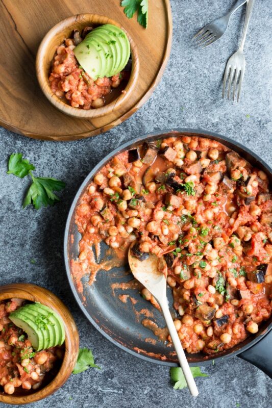 vegan bean and aubergine casserole in a skillet and served in two plates topped with avocado.