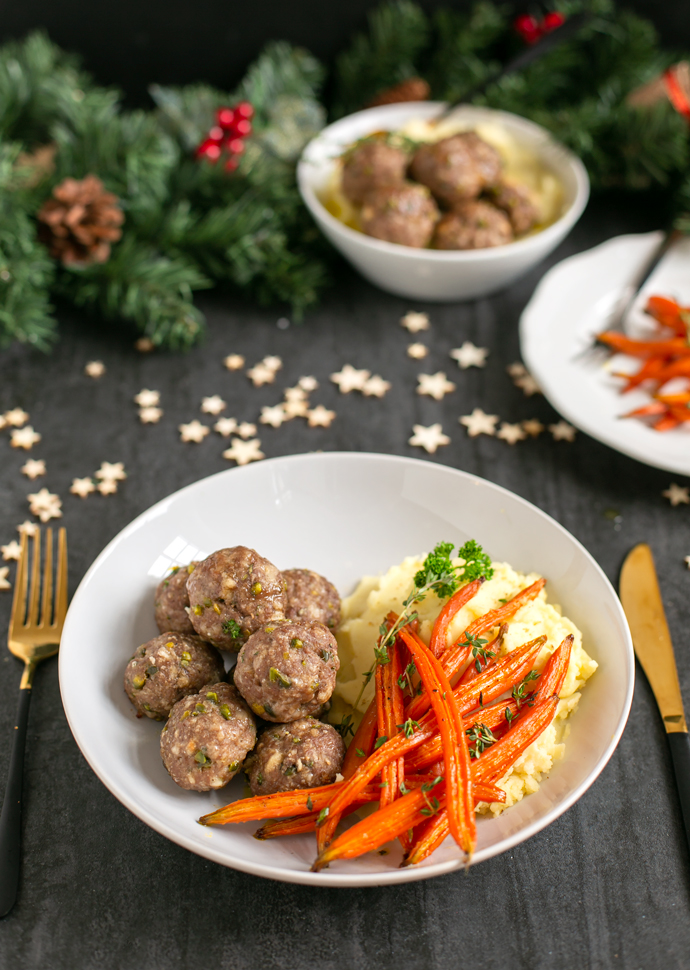 pistachio lamb meatballs served on a white dish together with glazed carrots and mashed potatoes