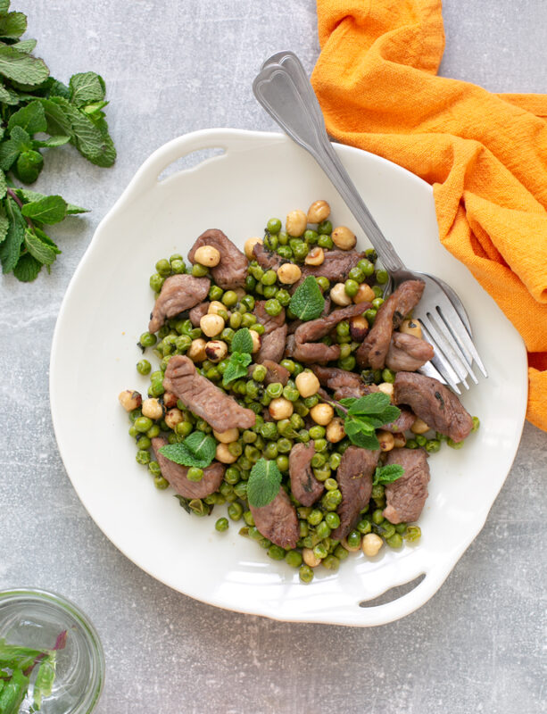 Air Fryer Mint Lamb with Toasted Hazelnut and Peas on a serving dish, next to a orange napkin, and fresh mint leaves