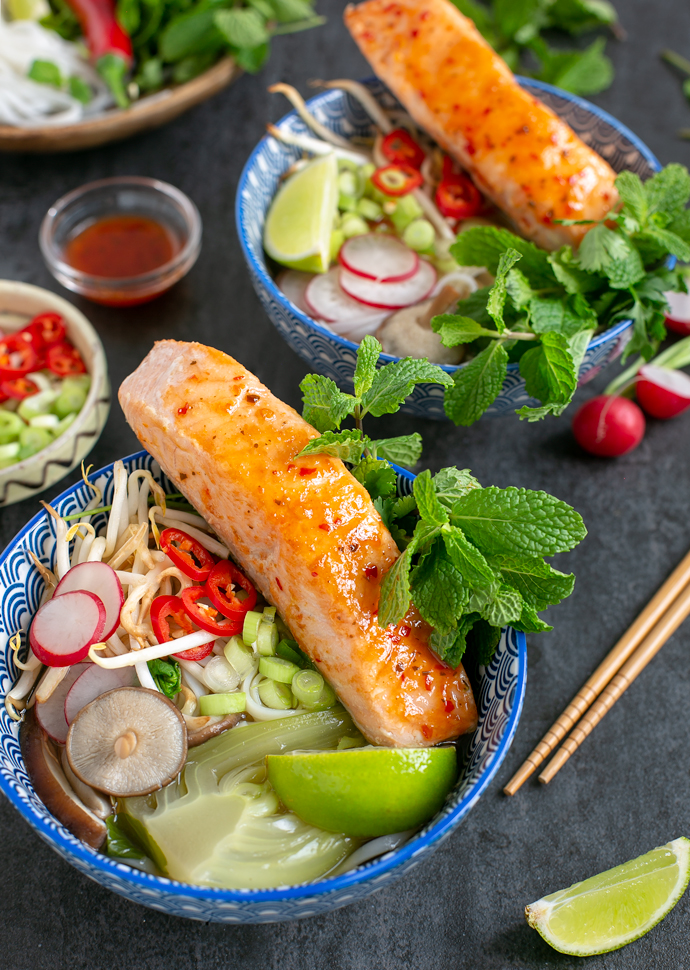 vietnamese pho with salmon served in two large bowls, toppings in small pot next to the bowls.