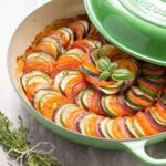 Easy Ratatouille in a large green cast iron shallow pan with lid on the side, bunch of thyme sprigs on the left side and a green napkin on the top right side.