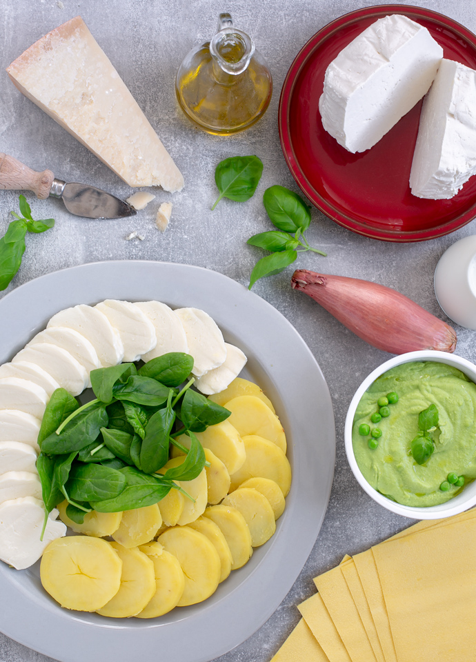 vegetarian lasagna ingredients: italian hard cheese, ricotta, shallot, milk, pea pesto, lasagna sheets, sliced potatoes, sliced mozzarella, spinach and basil leaves