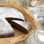 italian water cake with a slice of cake in evidence, water jug cookies cutters and sugar in a sieve on the side