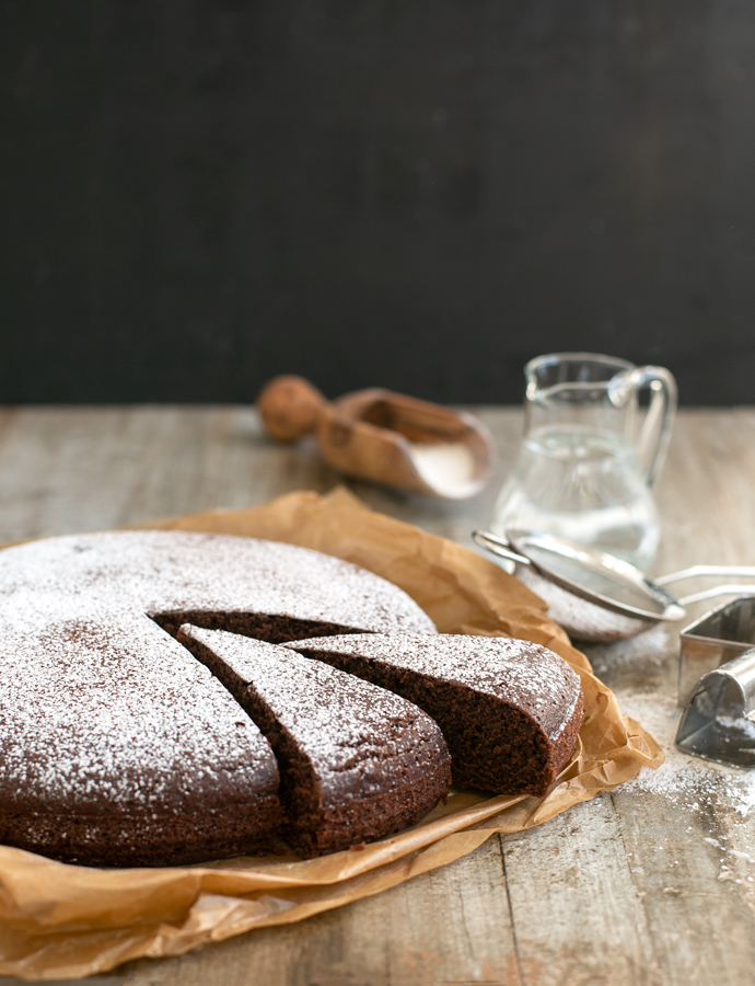 water cake with two slices cut. Sifter, water jug, spoon with flour in the background as decoration.