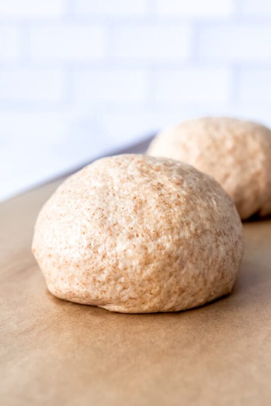 two whole wheat pizza doughs on a wood board.