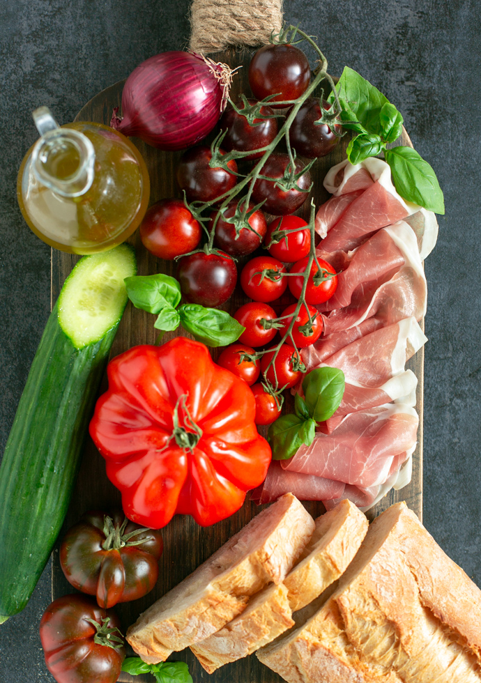 panzanella salad ingredients: olive oi, red onion, tomatoes, cucumber, bread parma ham slices and basil leaves.