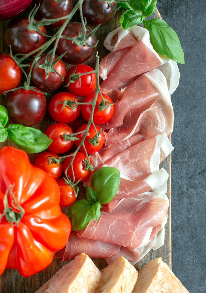 panzanella ingredients: parma ham slices, basil leaves, tomatoes.