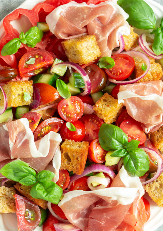 close up of panzanella salad with parma ham, bread cubes, tomatoes, onion, cucumber and basil leaves