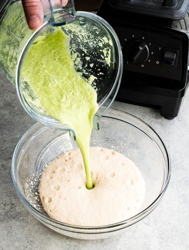 hand slowing pouring zucchini cream into the pizza dough place in a glass bowl.